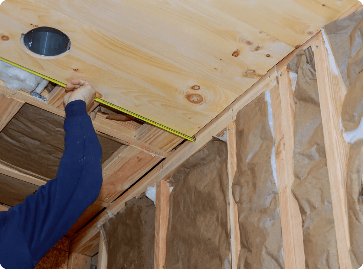 Worker measuring ceiling board with tape measure